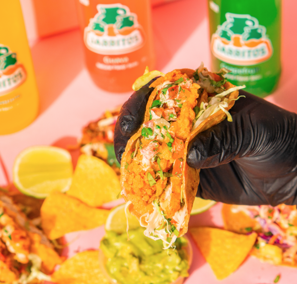 Taco holdt i hånden ved siden af mexicanske sodavand